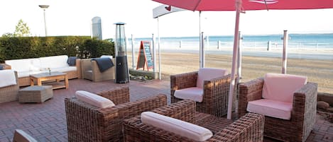 Wicker furniture with cushions, a red umbrella, and a view of the beach.