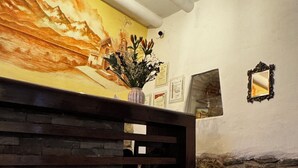 A room with a wooden slatted headboard, a table with magazines and a black folder labeled 'UCHU', a wall with a mural, and a stone wall. - Huascaran Casa Boutique Cusco (Cusco)