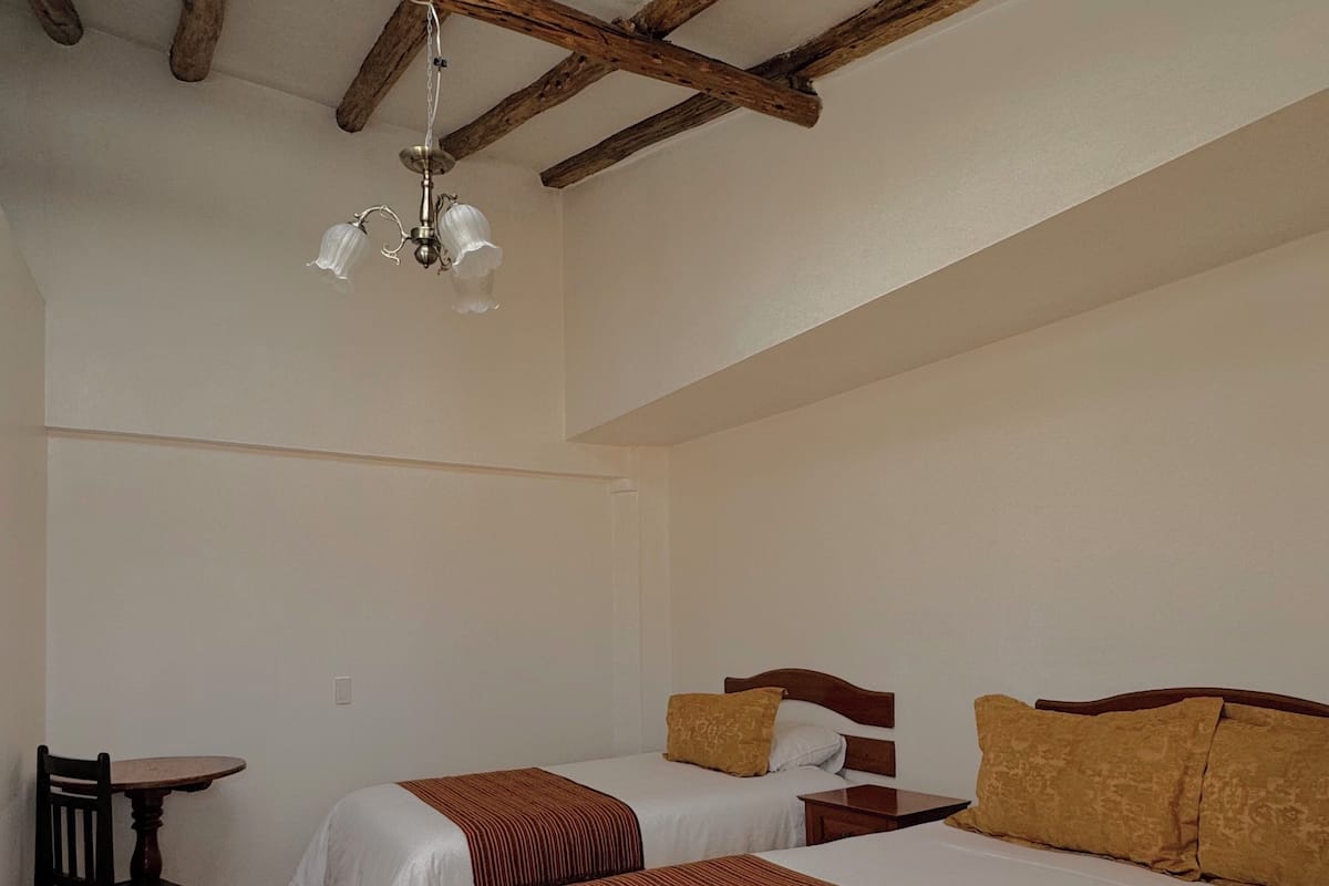 Quarto com duas camas, uma mesa de madeira e um lustre.
