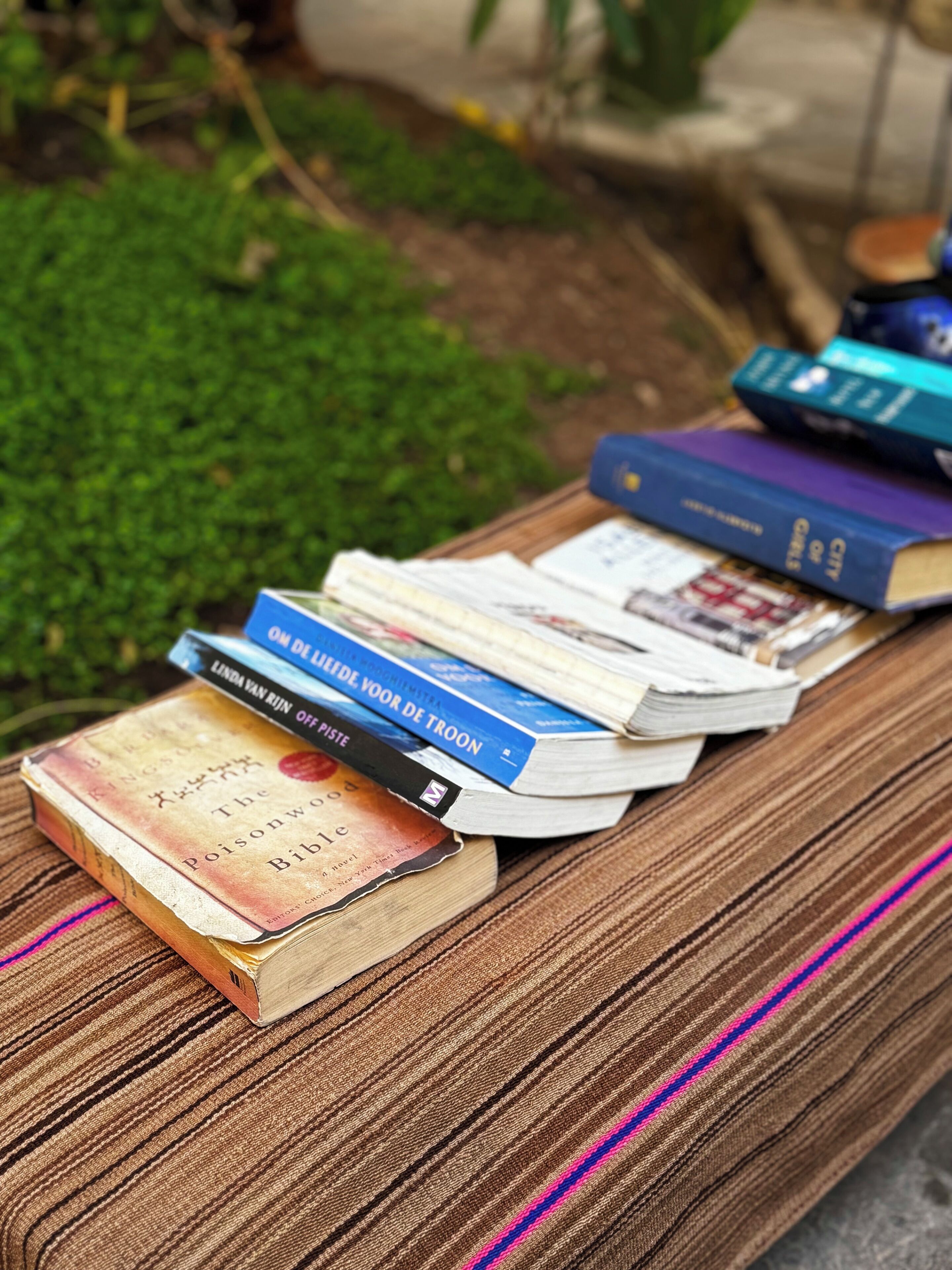 A stack of books on a wooden bench outdoors.
