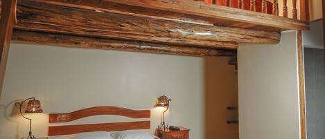 A bedroom with a wooden bed, two bedside tables with lamps, a red blanket, and a wooden chair.