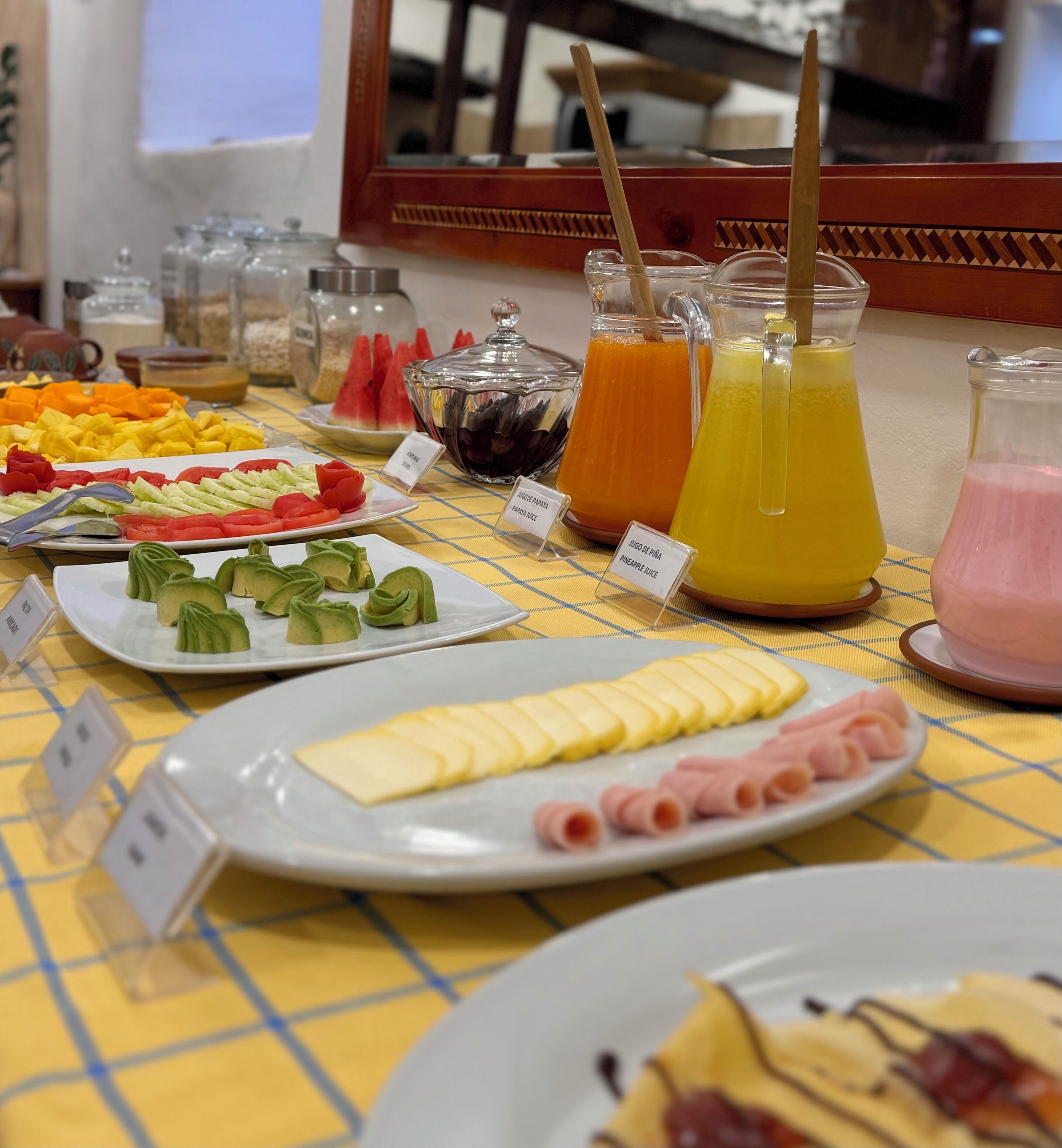 A buffet table with various food items and drinks, including sliced fruits, vegetables, cheese, and meats, with labels indicating the type of food.