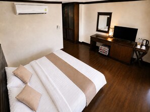 Ett hotellrum med en säng, en tv, ett skrivbord med en lampa och en luftkonditioneringsanläggning.
