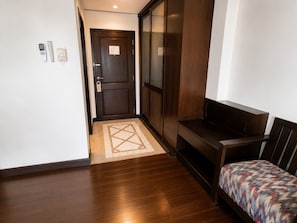 Un couloir d’hôtel avec un plancher en bois, un banc, une porte avec une pancarte et une petite table sur laquelle se trouvent un téléphone et une télécommande.