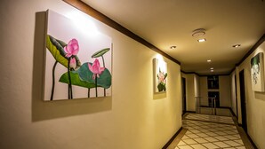Een gang met betegelde vloer, kunstwerken in lijsten aan de wanden en inbouwverlichting.