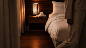 Habitación de hotel con cabecera de madera, mesita de noche con una lámpara, una taza y un libro.