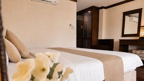 Een hotelkamer met een bed, een bureau, een spiegel en een wandairconditioner.