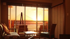 A room with a view of a bridge at sunset, featuring a sofa, chairs, and a table.