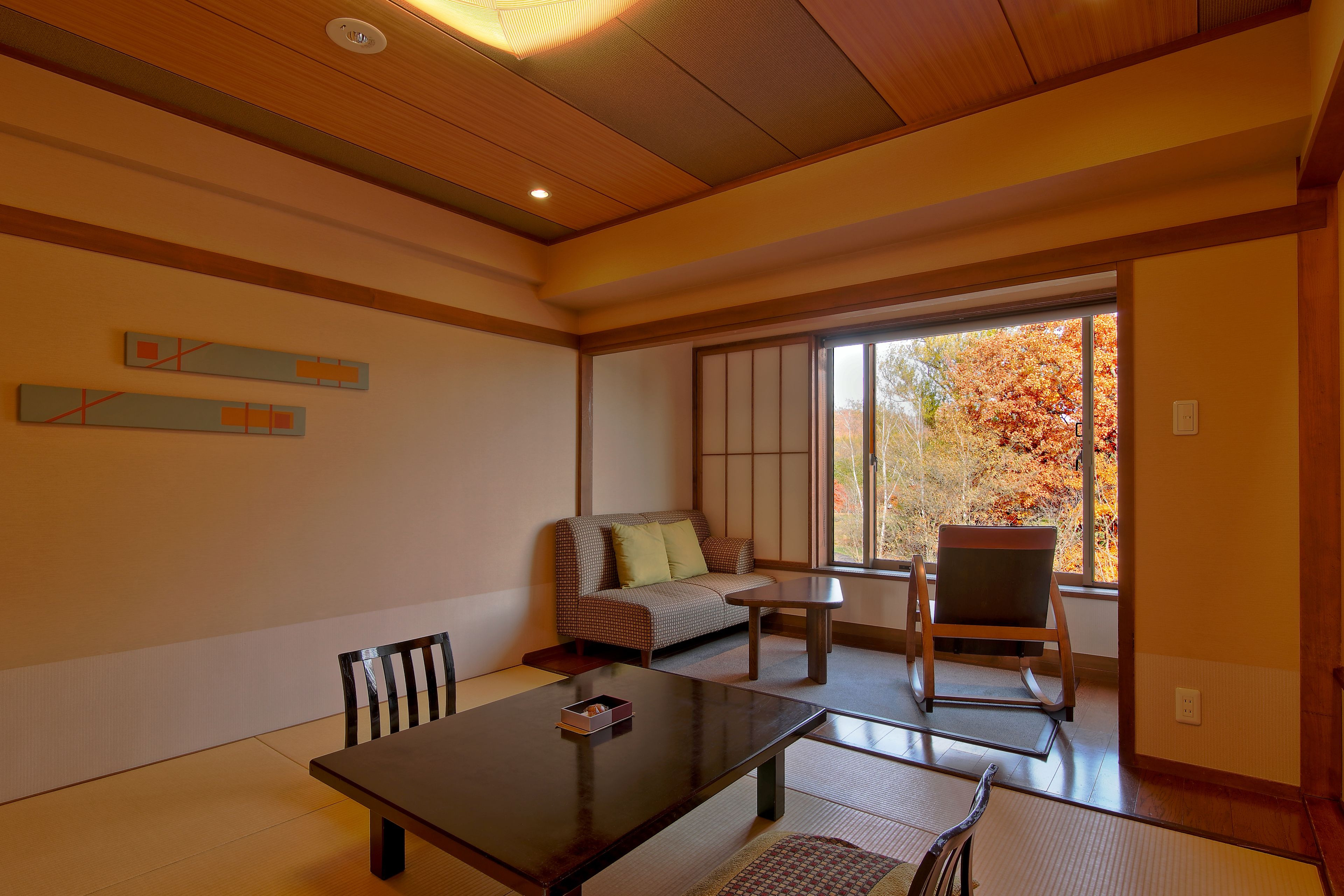 Une pièce de style japonais traditionnel, avec un sol recouvert de tatamis, une basse table en bois, un canapé et un fauteuil.
