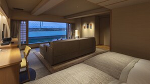 A hotel room with a sofa, a desk, a chair, and a view of a bridge.