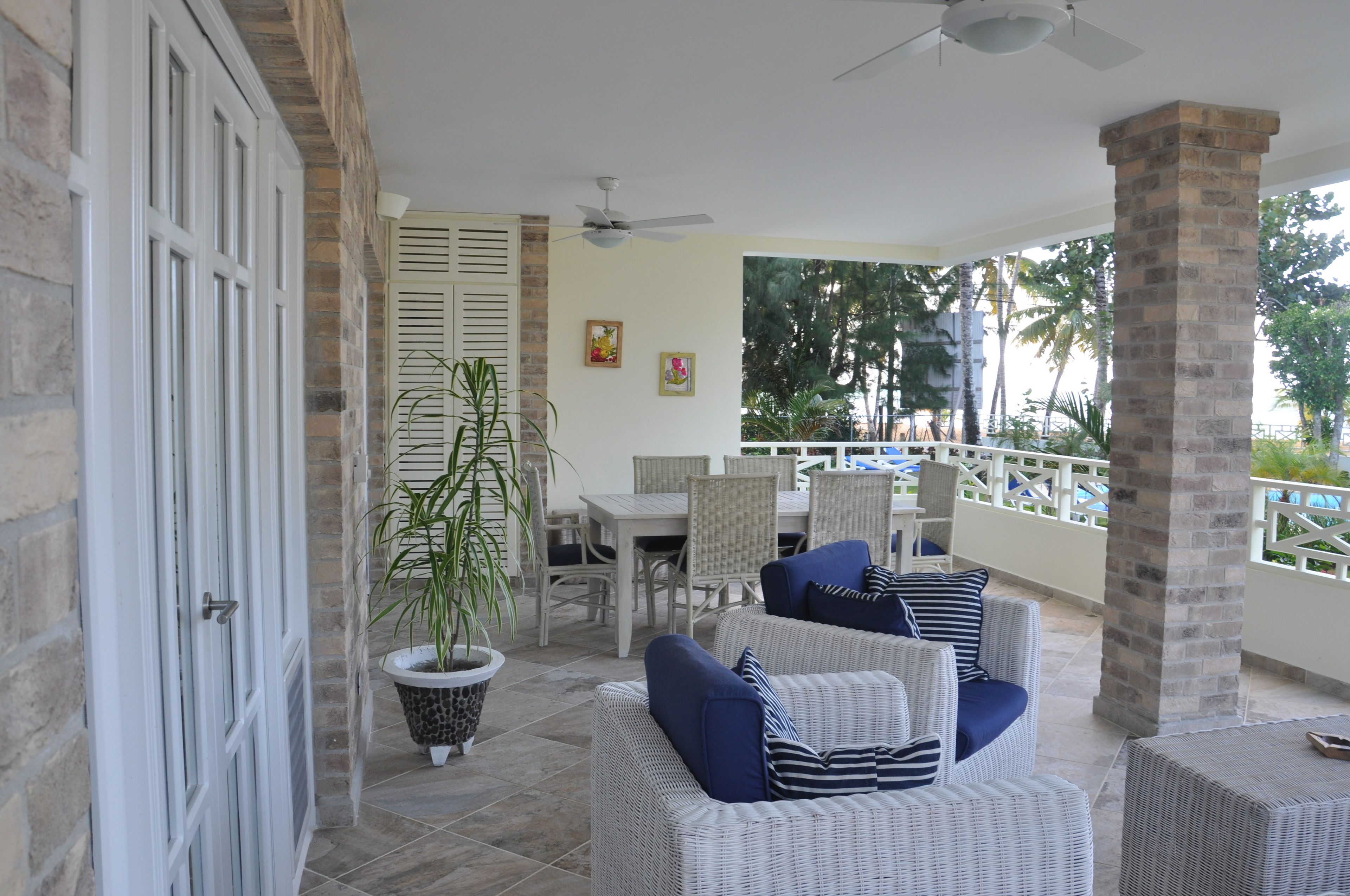 An outdoor patio with wicker furniture, a potted plant, and a dining area.