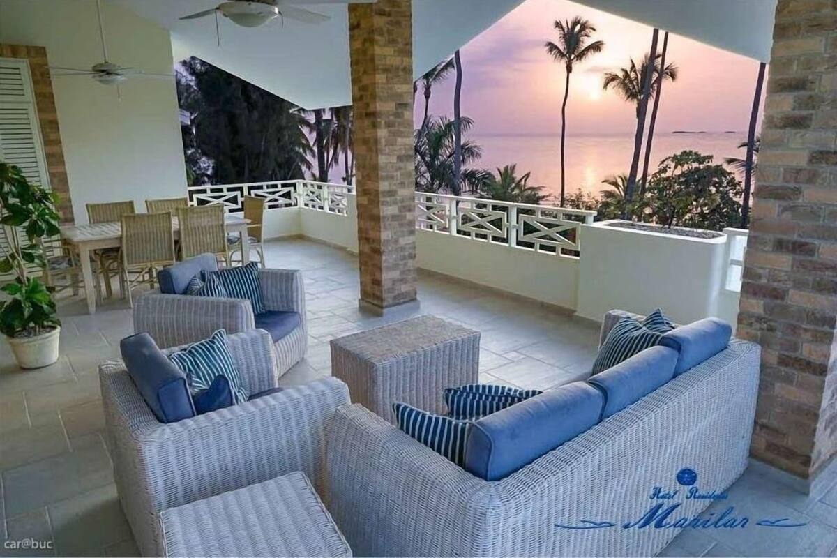 A balcony with wicker furniture, a view of the sunset, and palm trees.