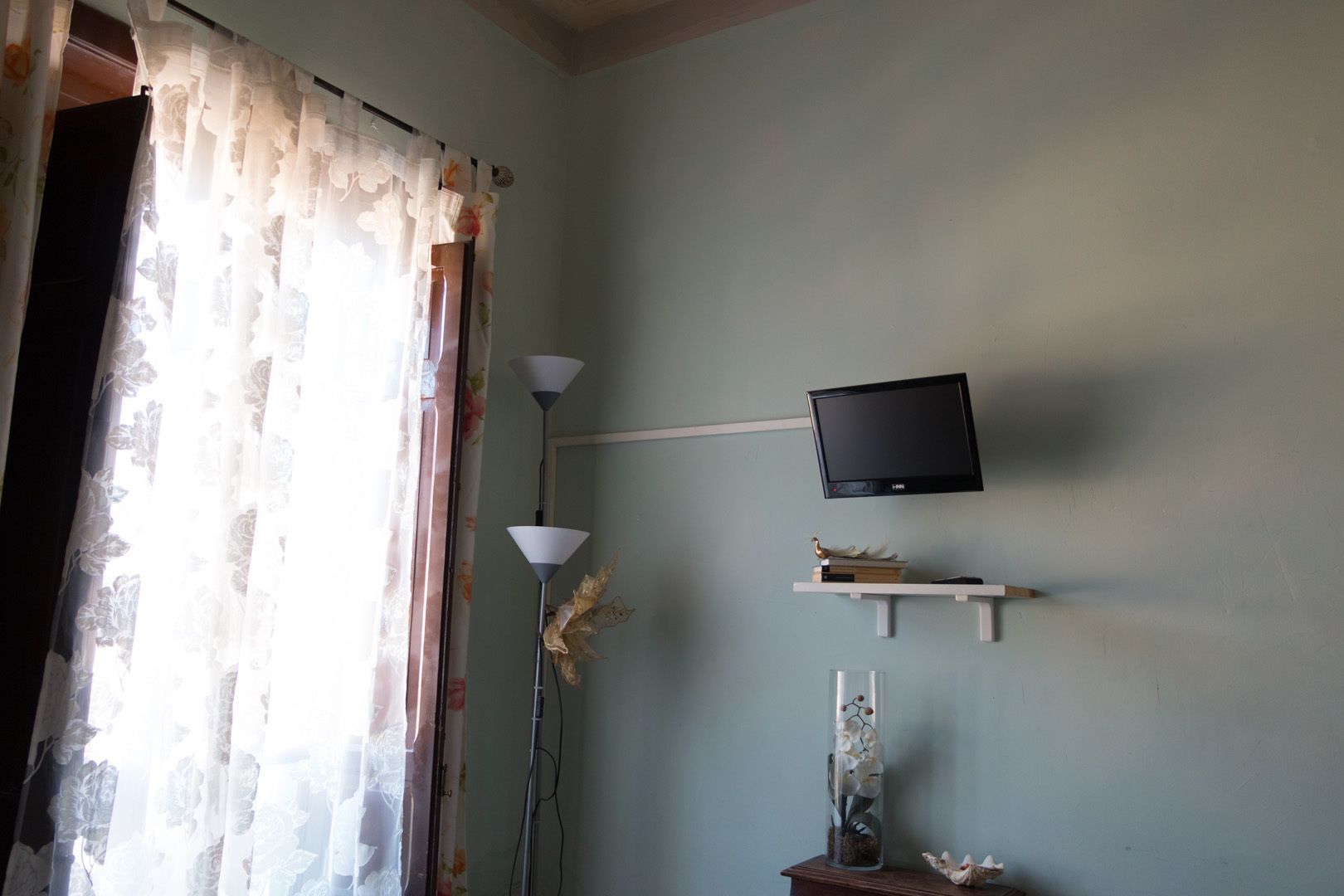 Una stanza con una televisione a parete, una lampada e uno scaffale con libri e oggetti decorativi.