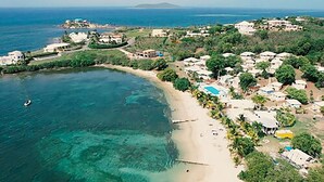 An aerial view of a coastal area with a beach, clear waters, and a mix of residential buildings and greenery. - Bungalows on the Bay (Christiansted)