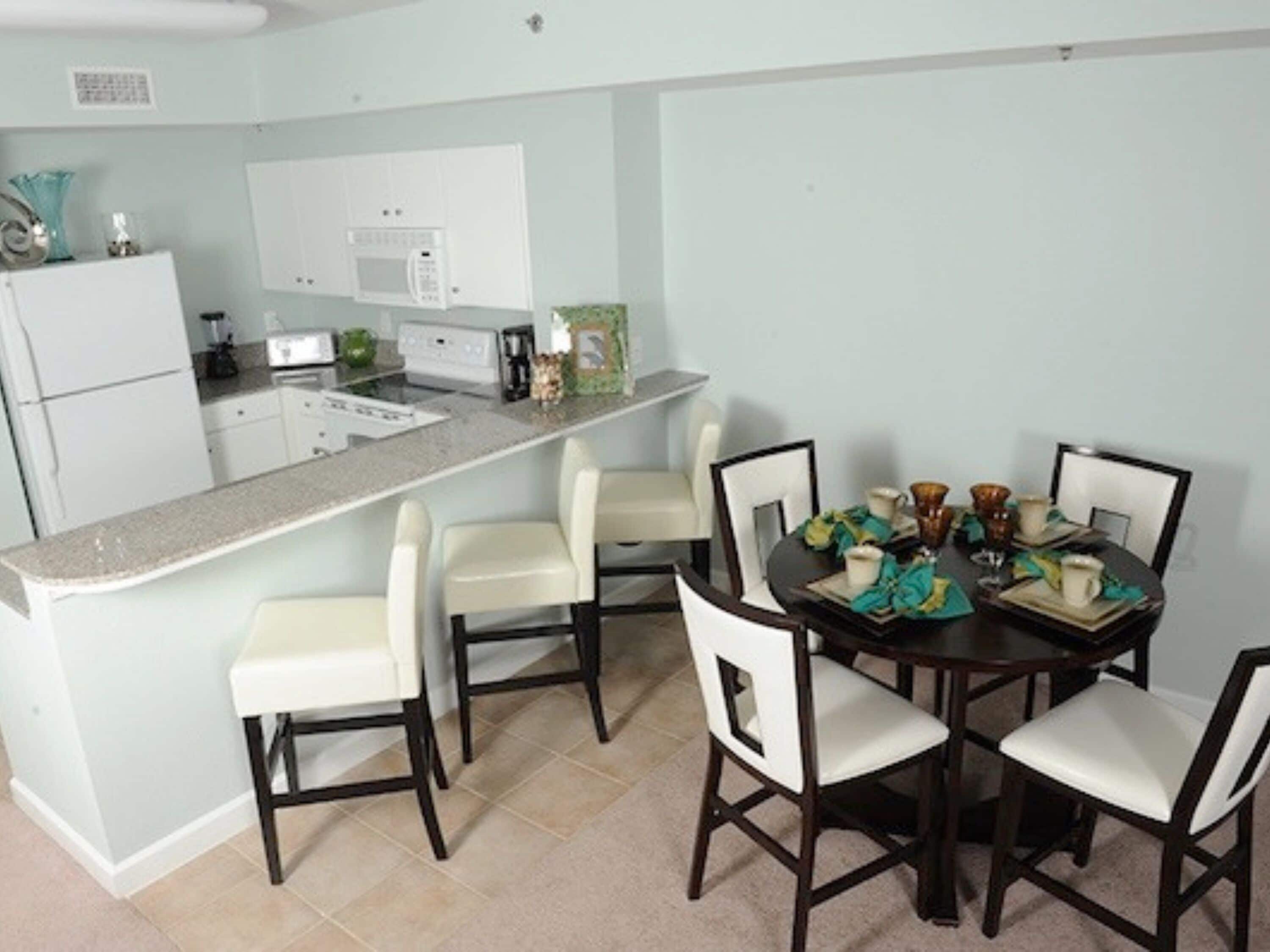 A compact kitchen with a central island, white appliances, and a dining area with four chairs.
