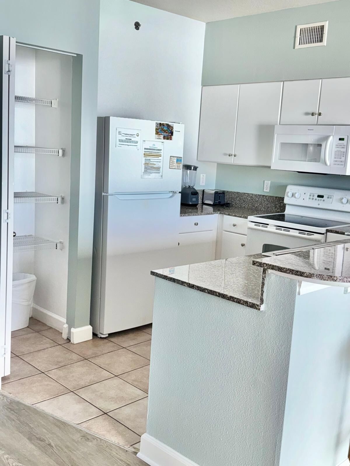 Una cocina moderna con armarios blancos, un refrigerador empotrado, microondas, estufa y una isla con cubierta de granito.