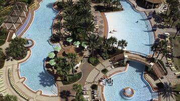 A large, multi-level swimming pool complex with various water features, surrounded by palm trees and sun loungers.