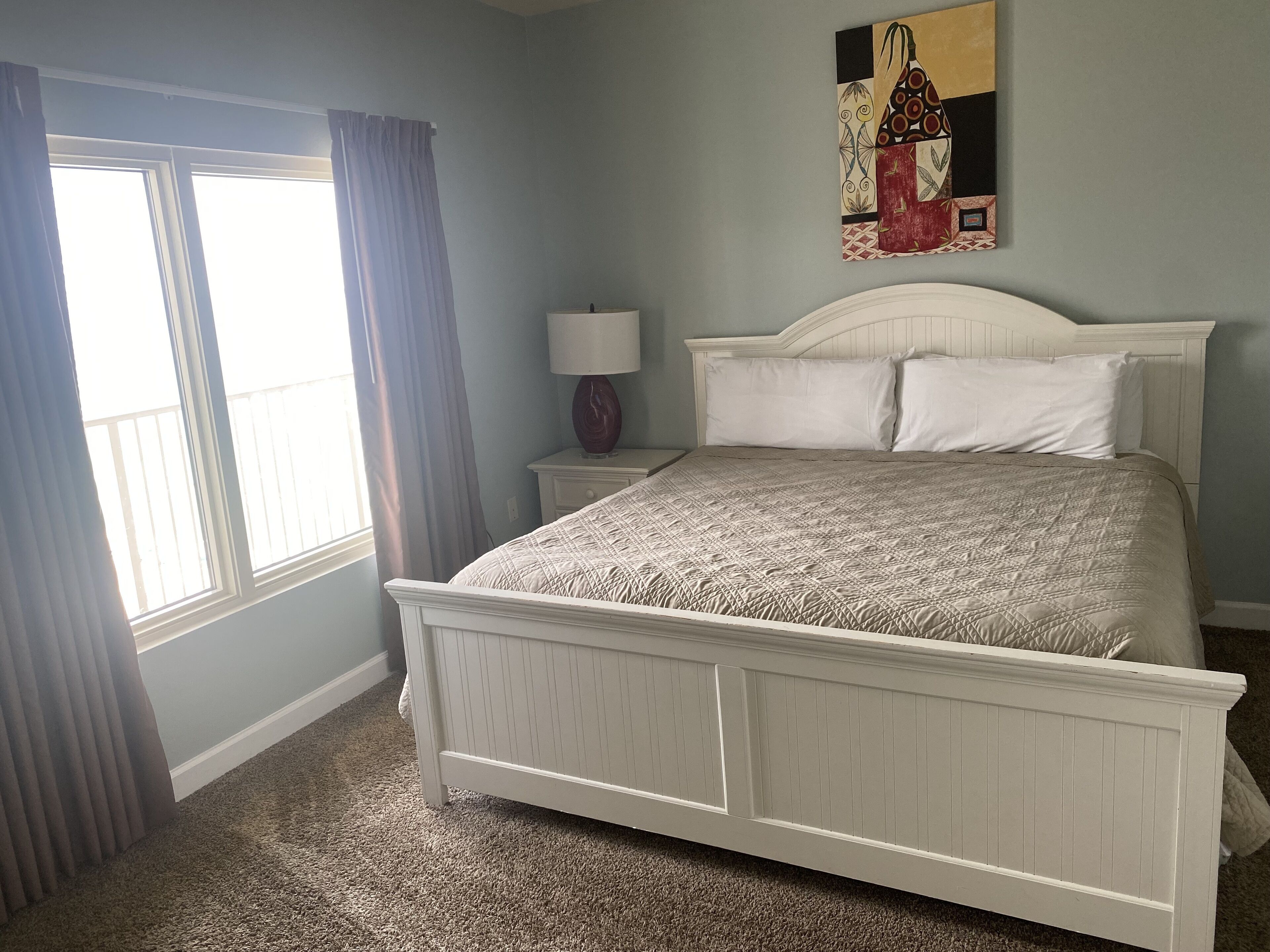 A bedroom with a bed, a nightstand, a lamp, and a painting on the wall.