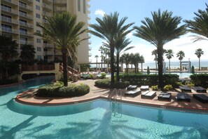 A resort pool area with palm trees, lounge chairs, and a view of the ocean. - Shores of Panama Beach Resort (Panama City Beach)