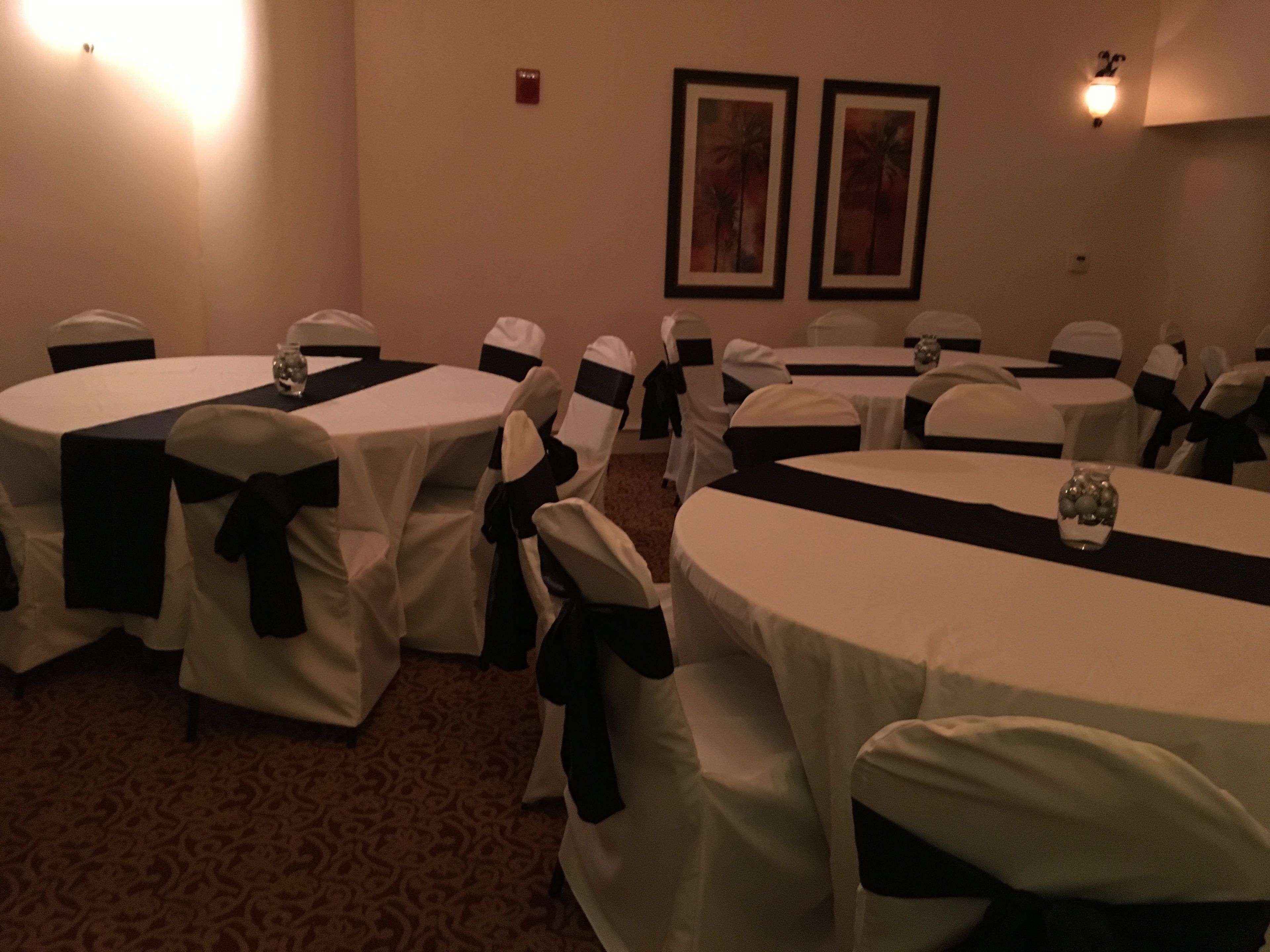 A conference room with round tables, each covered with white tablecloths and black sashes, and chairs with white covers and black sashes.