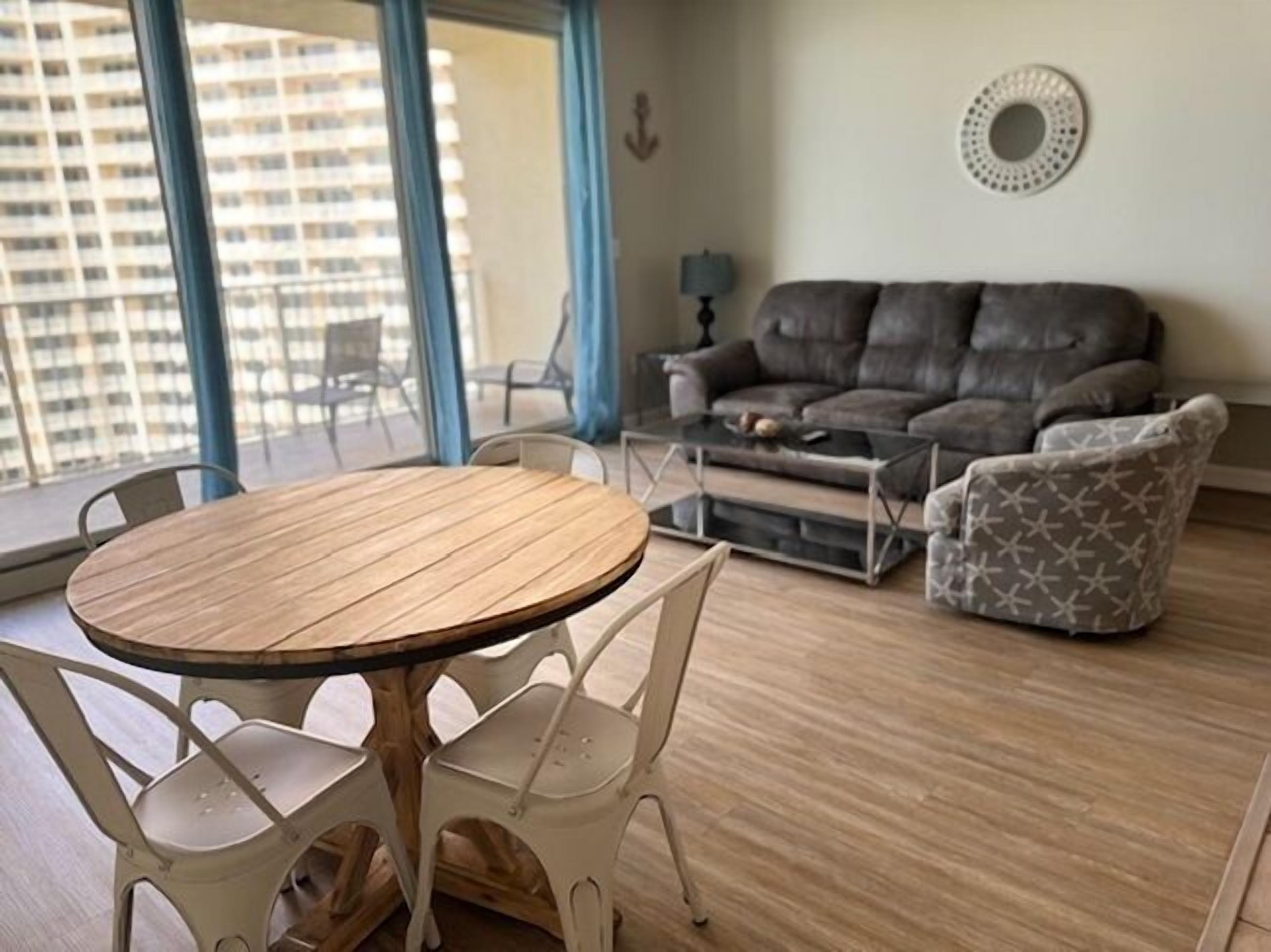 Un salon avec un canapé gris, un fauteuil à motifs, une table ronde en bois entourée de chaises et une table basse.