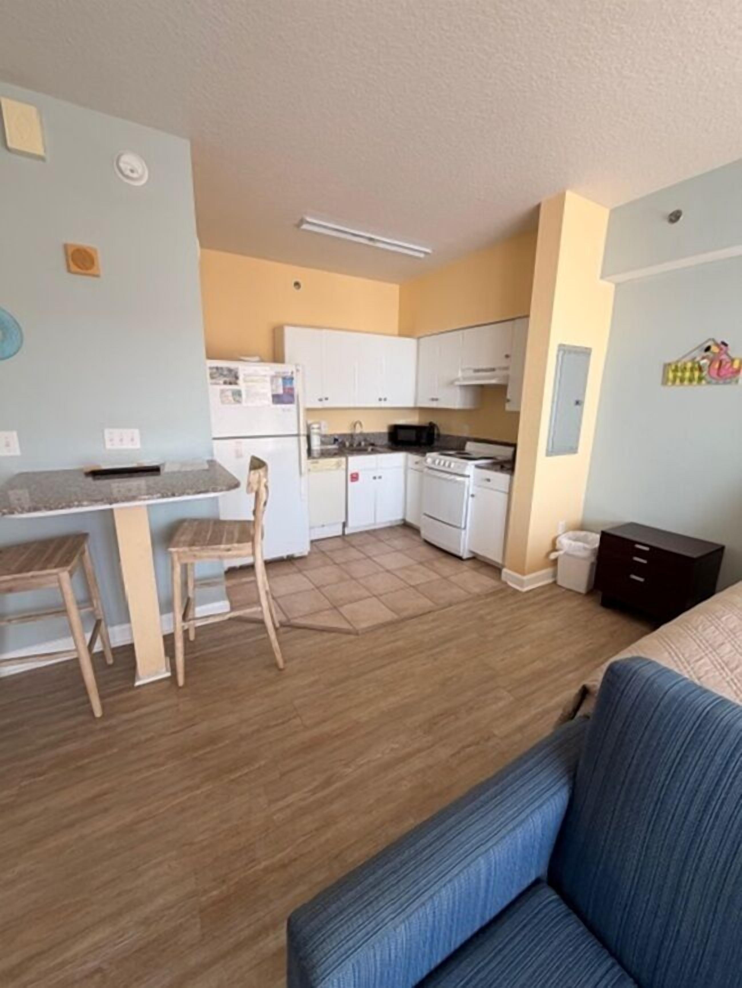 A compact living space with a kitchenette, a dining area with two stools, a sofa, and a small cabinet.