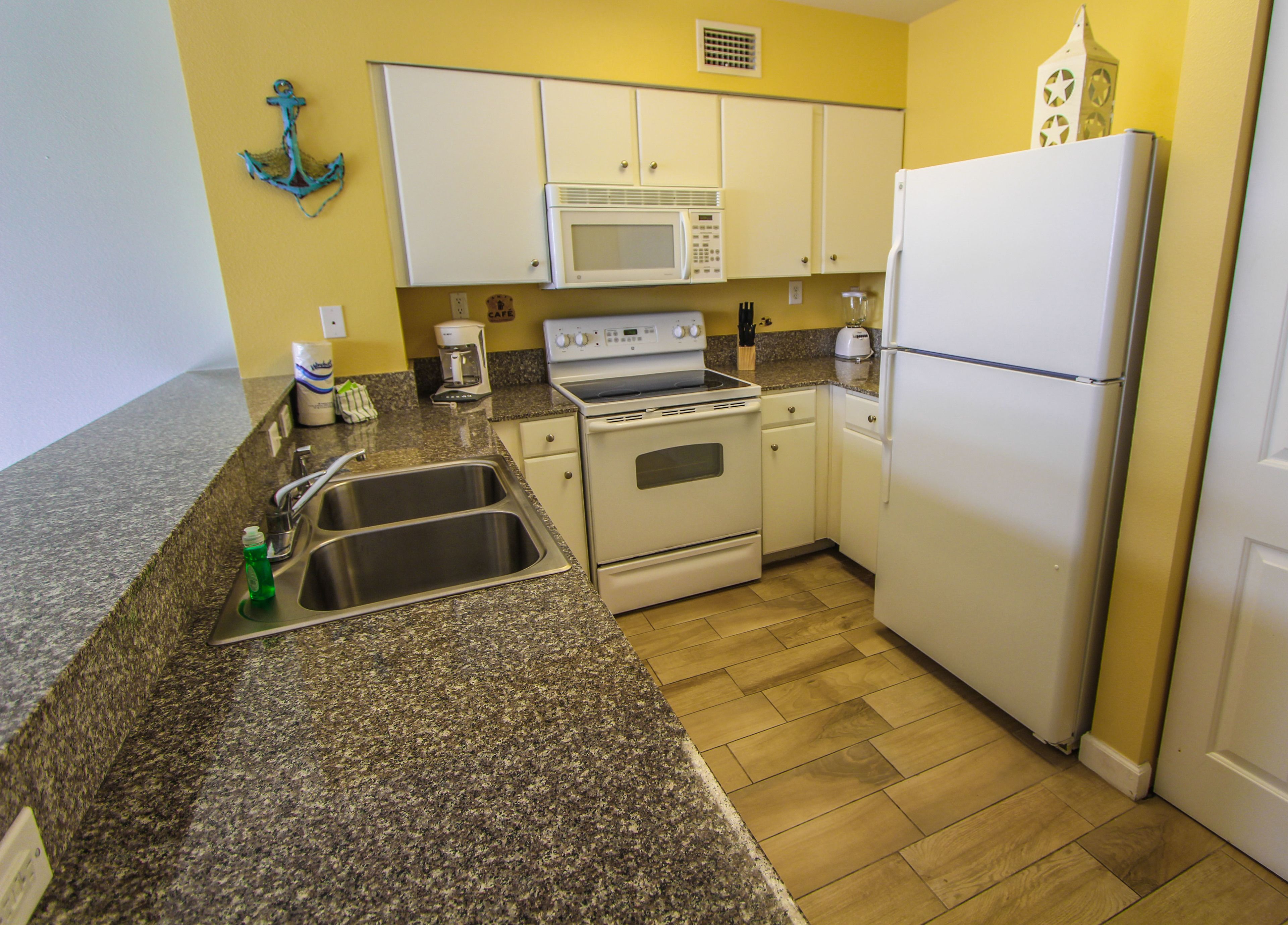 A compact kitchen with white appliances, granite countertops, and a yellow wall.