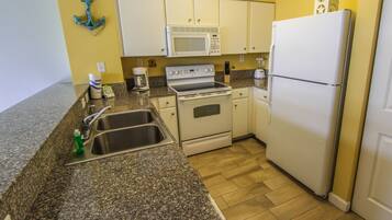 A compact kitchen with white appliances, granite countertops, and a yellow wall.