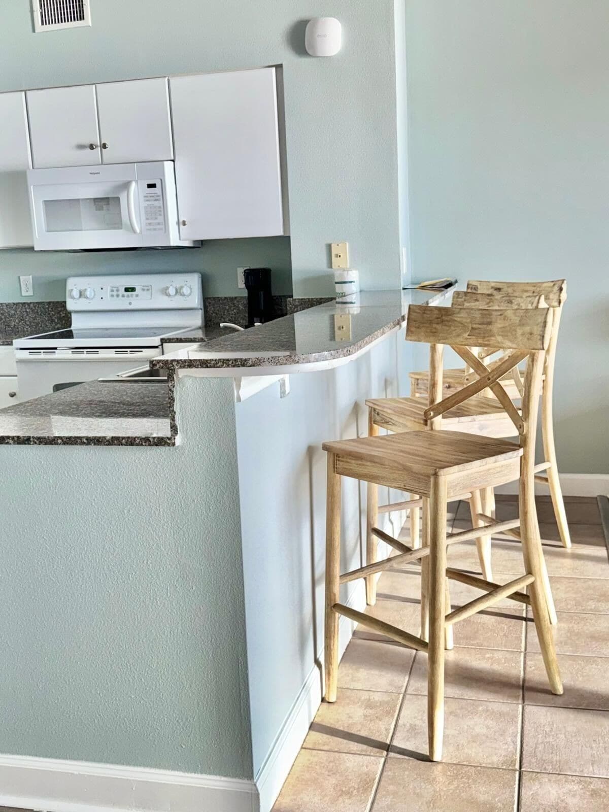 A modern kitchen with white cabinets, a microwave, a stove, and a wooden chair.