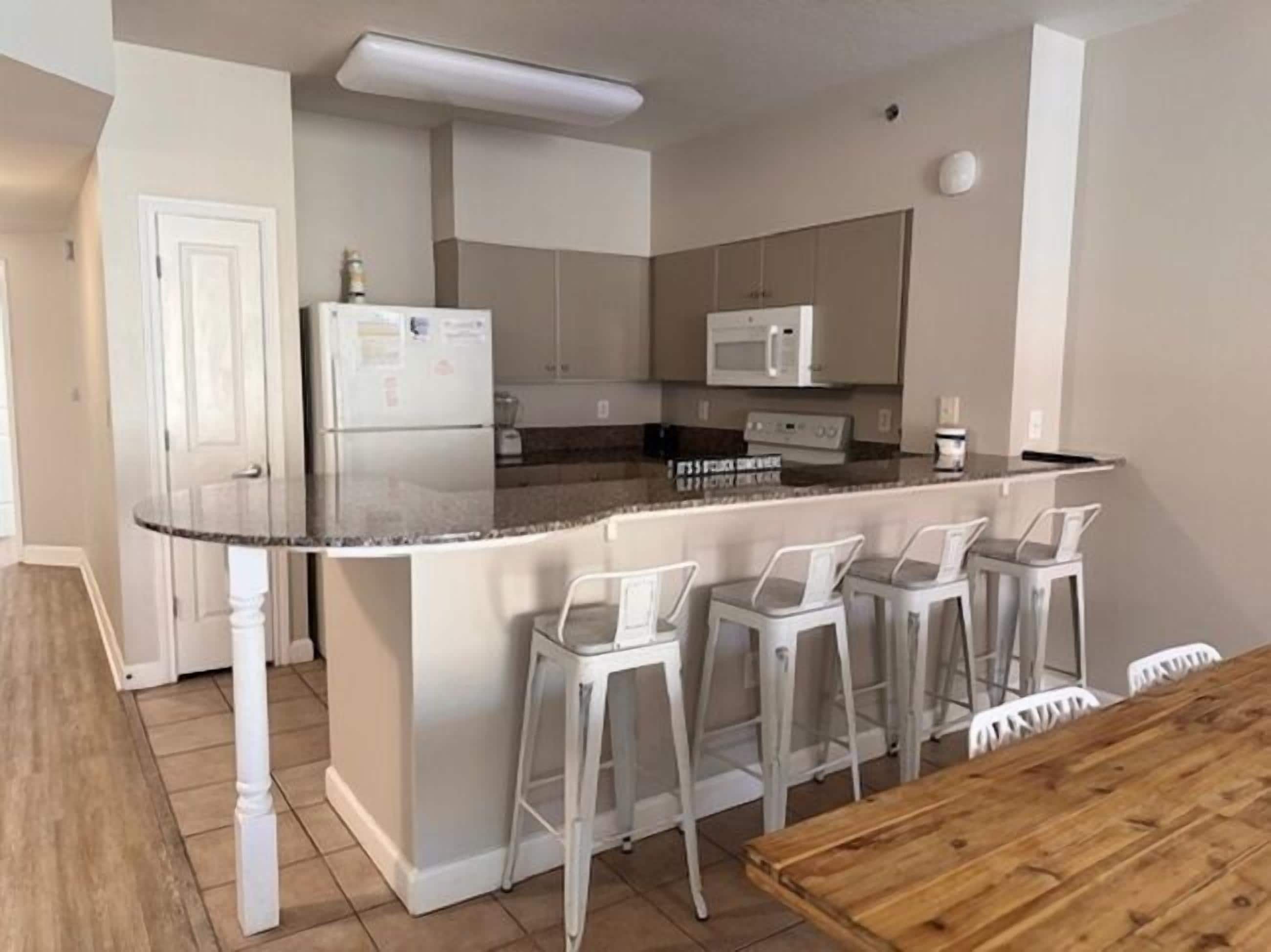 A kitchen with a central island, white bar stools, and a wooden dining table.