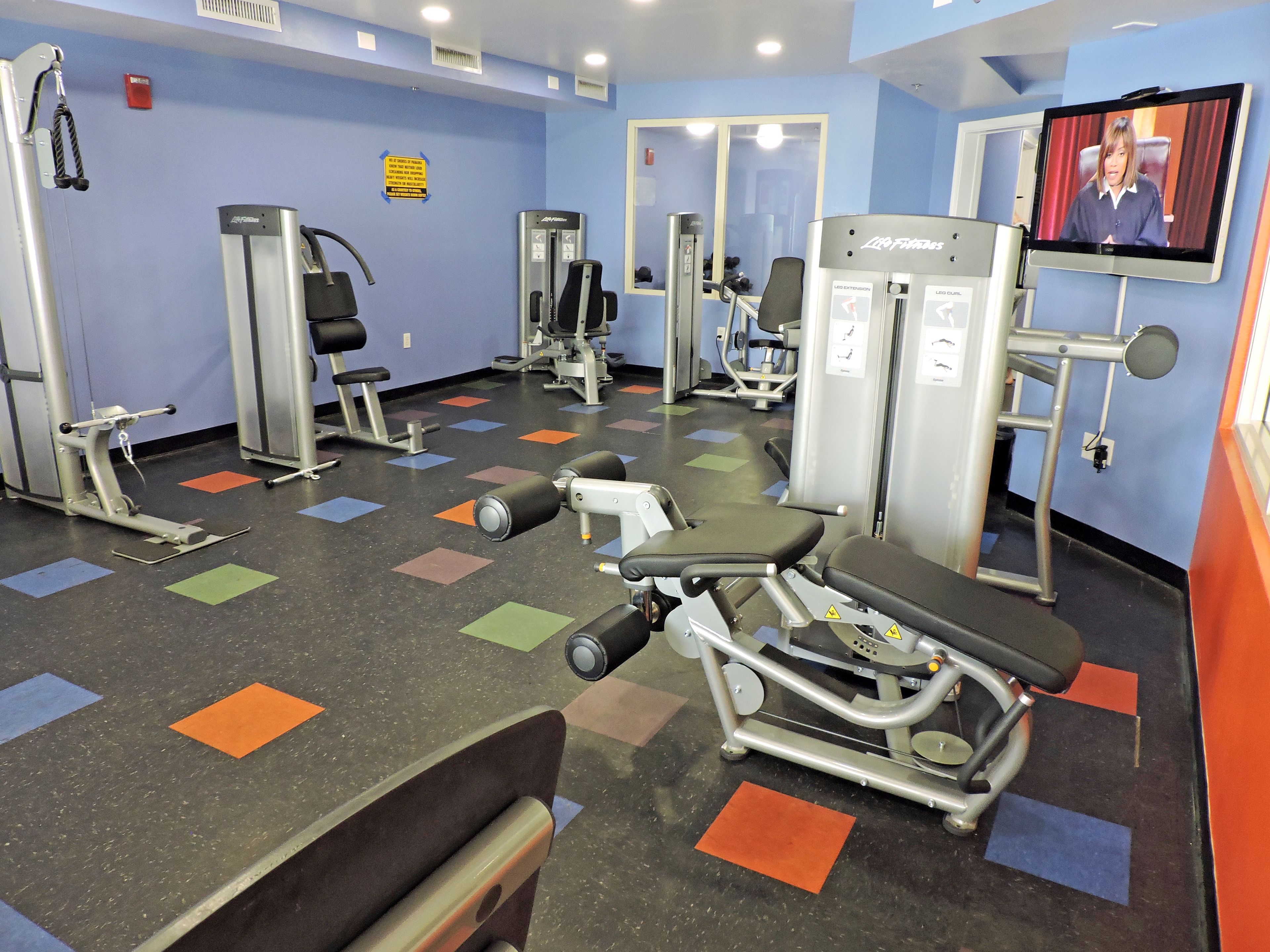 Une salle de sport équipée de divers appareils d’exercice, d’un téléviseur et d’un miroir.
