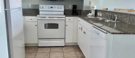 A compact kitchen with white cabinets, a microwave, an oven, a sink, and a coffee maker.