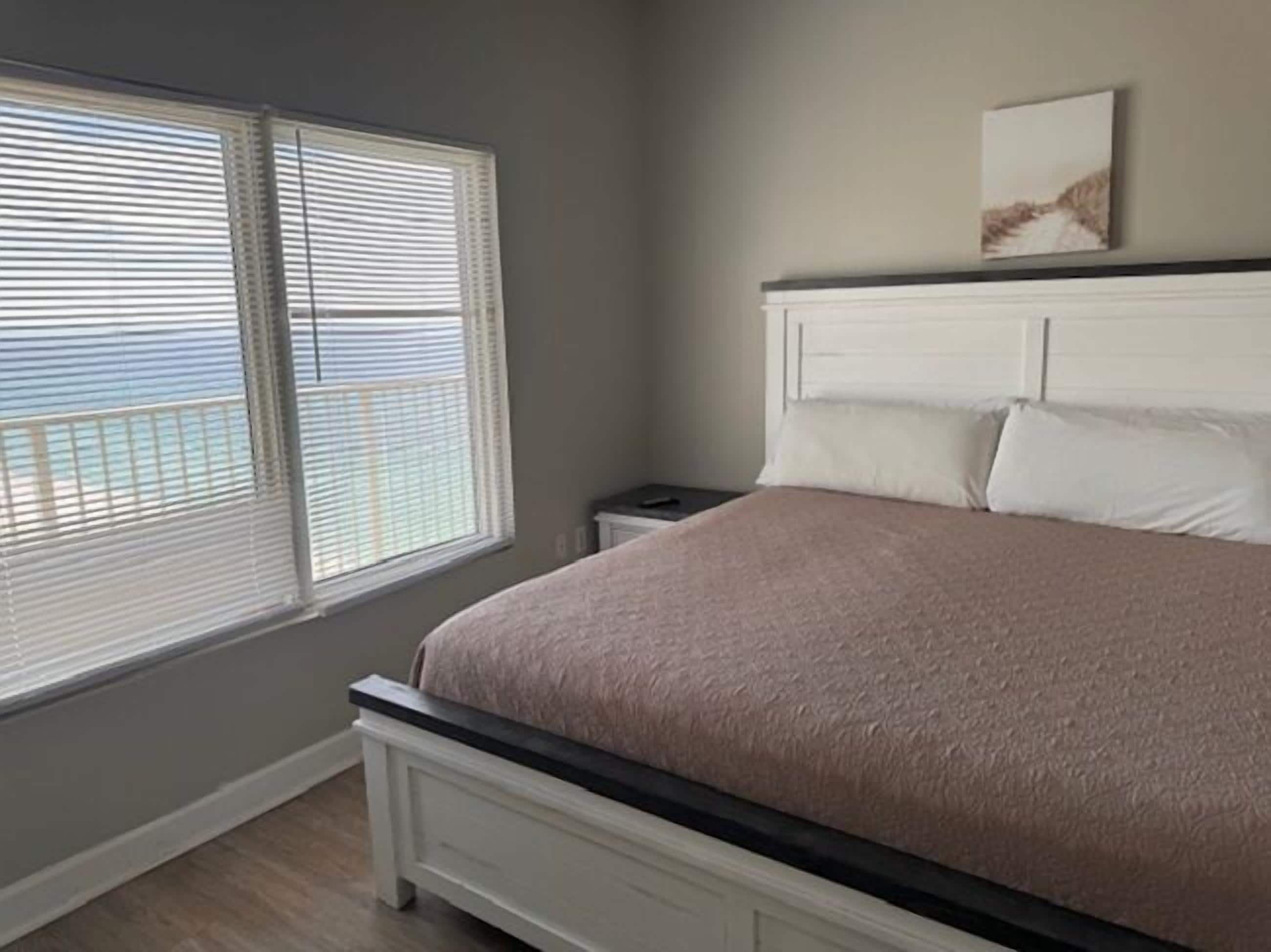 A bedroom with a bed, a nightstand, and a window with blinds.