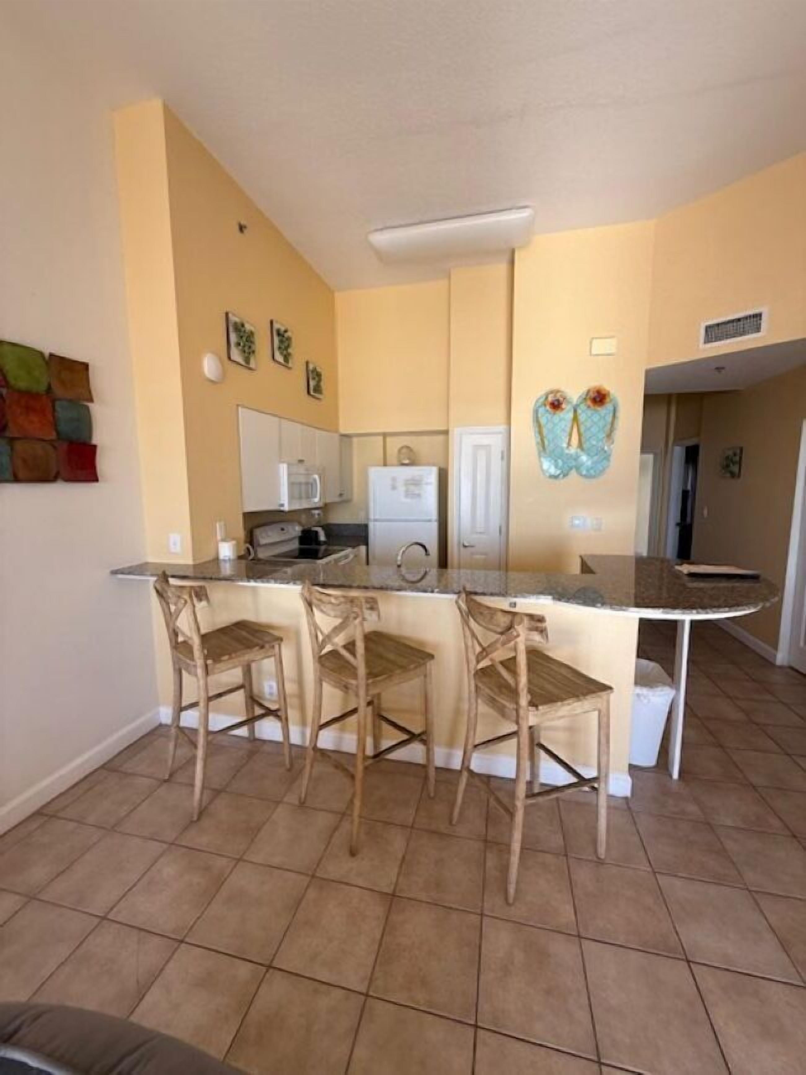 A compact kitchen with a central island, three bar stools, and a microwave.