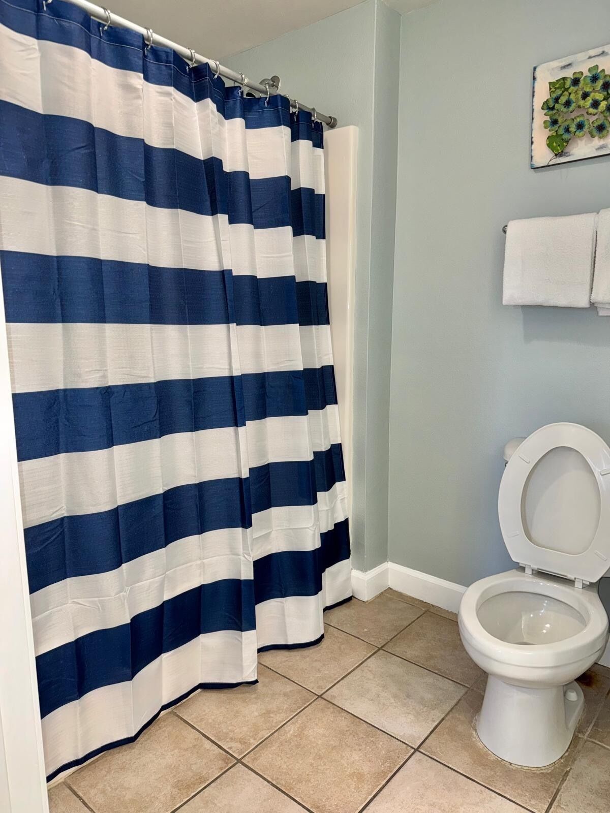 A bathroom with a striped shower curtain, a toilet, and a towel rack with a towel.