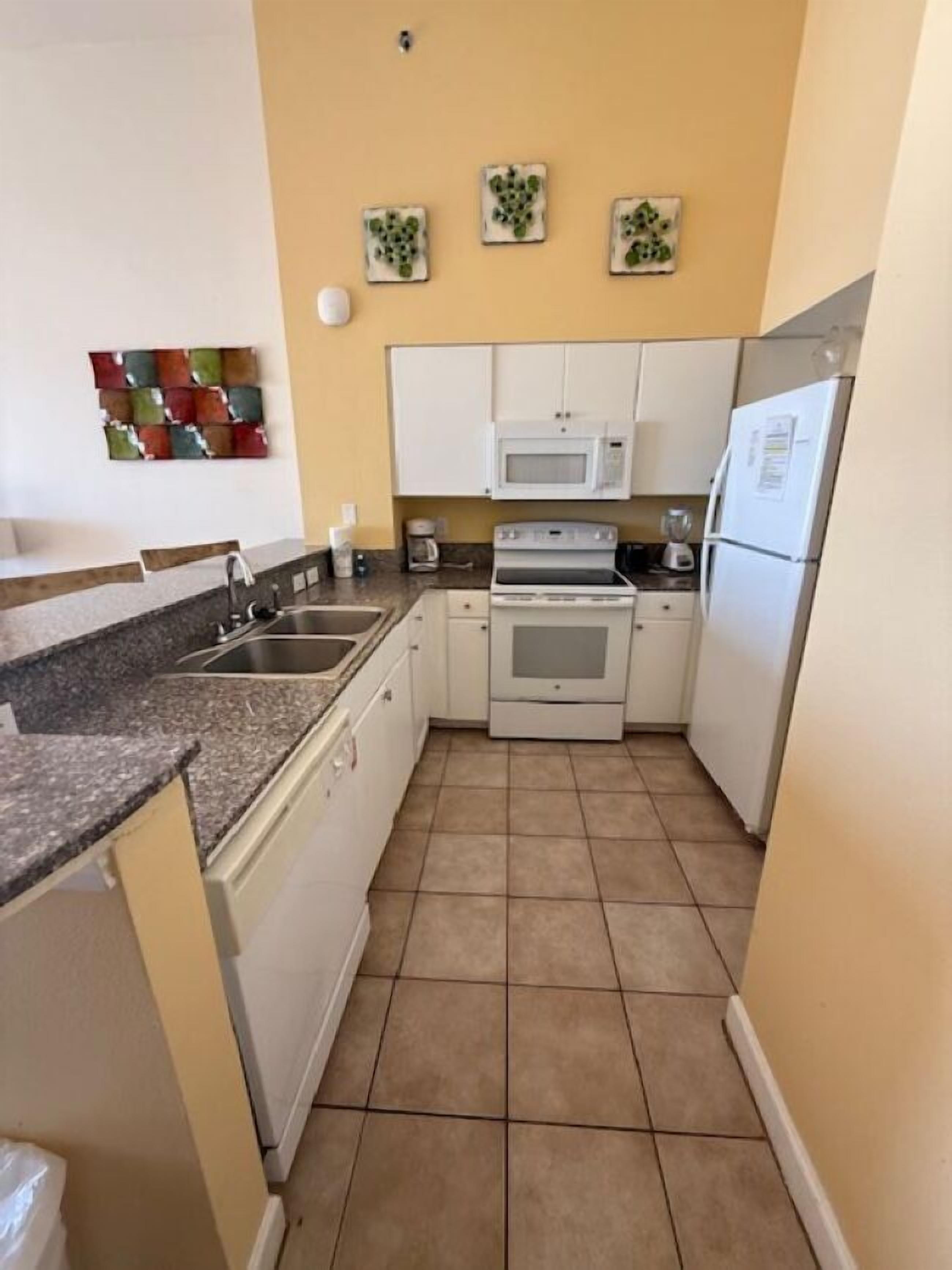 Una cocina compacta con gabinetes blancos, microondas, horno y refrigerador. Hay tres adornos en la pared sobre la encimera.