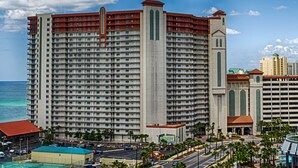 A high-rise hotel with multiple floors, a prominent central tower, and a pool area in the foreground. - Shores of Panama Beach Resort (Panama City Beach)