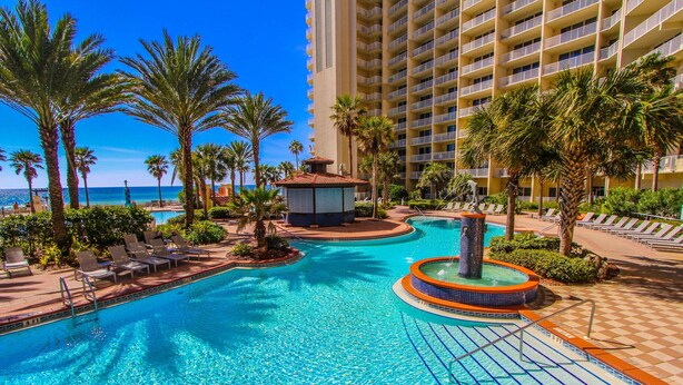 A hotel pool area with a circular hot tub, lounge chairs, palm trees, and a view of the ocean. - Shores of Panama Beach Resort (Panama City Beach)