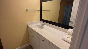 A bathroom with a white vanity, a large mirror with lights, and a towel rack.