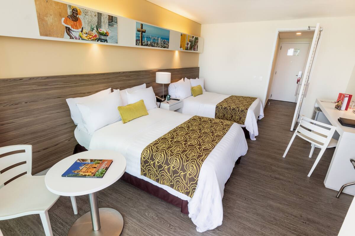 Habitación de hotel con dos camas, una mesita, una silla y una obra de arte en la pared.