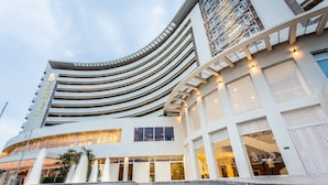 Un hotel moderno con fachada curva, varios balcones y una entrada destacada con una fuente.
