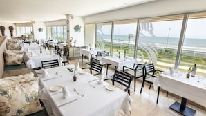 Un restaurante con varias mesas dispuestas para comer, grandes ventanales que ofrecen vistas al océano, y una decoración de diseño moderno.