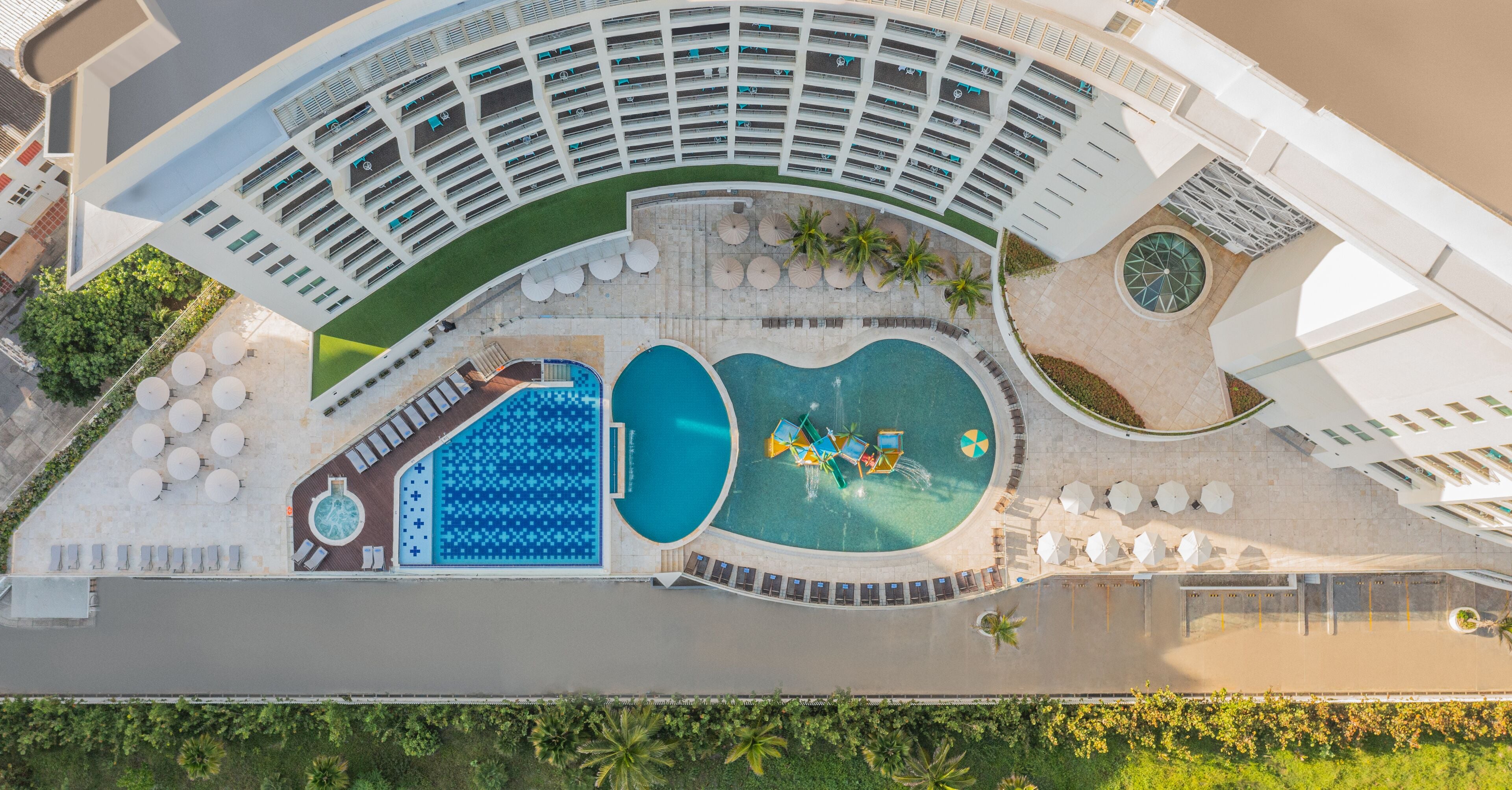 An aerial view of a hotel with multiple swimming pools, sun loungers, and a landscaped area with palm trees.