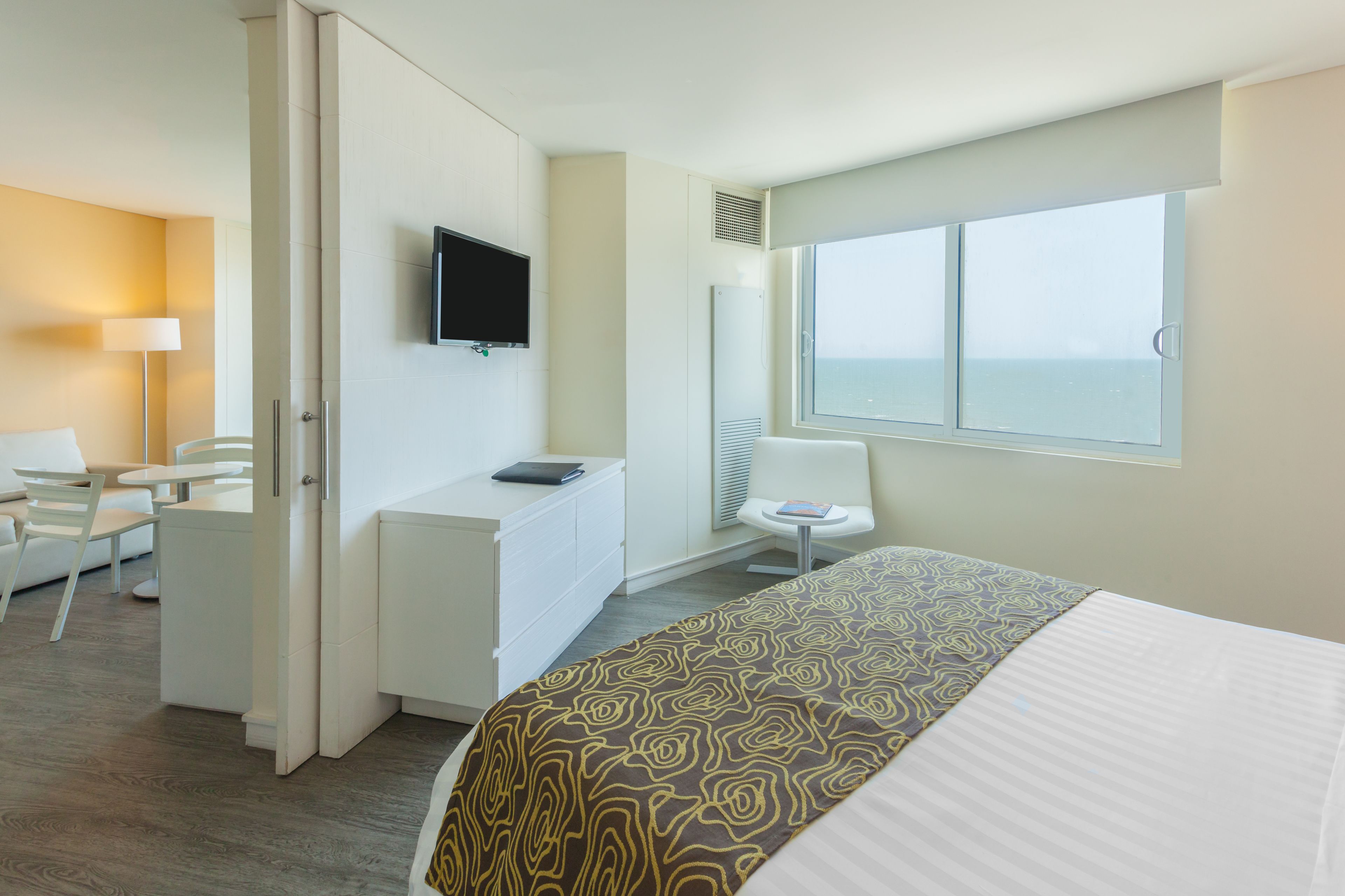 Quarto de hotel com cama, secretária, cadeira, televisão e janela com vista.