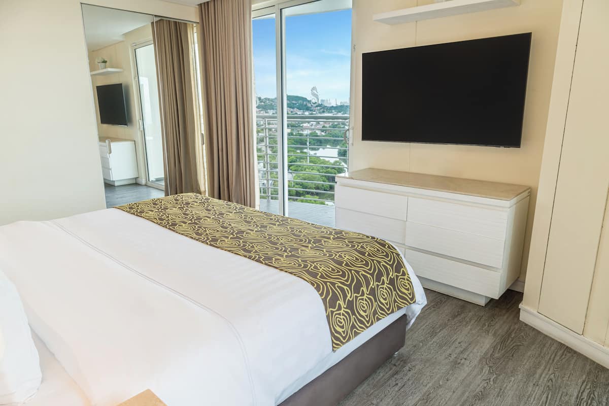 Habitación de hotel con una cama grande, un televisor de pantalla plana, un aparador y un balcón con vistas a la ciudad.