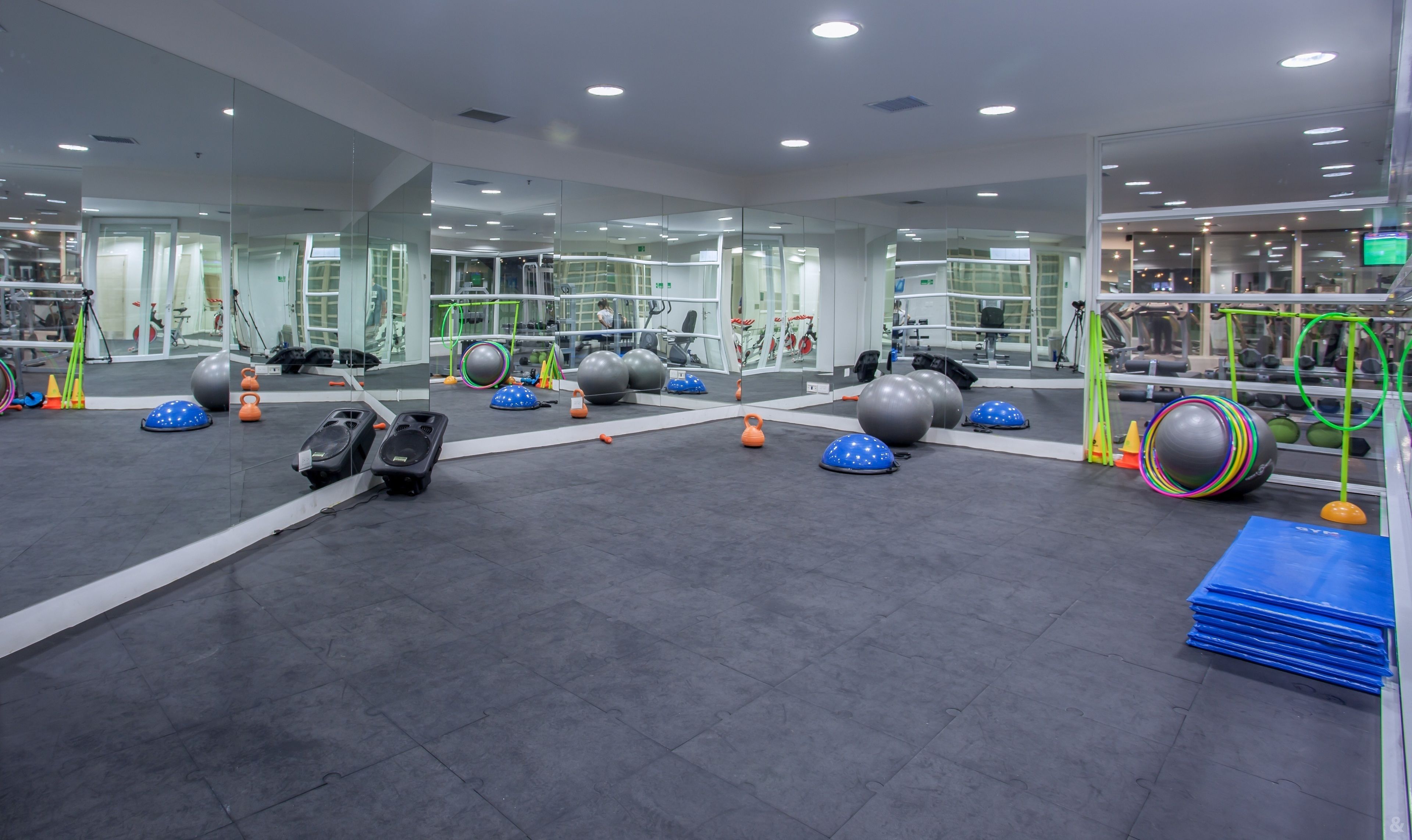 A gym with exercise equipment, mirrors, and a grey floor.
