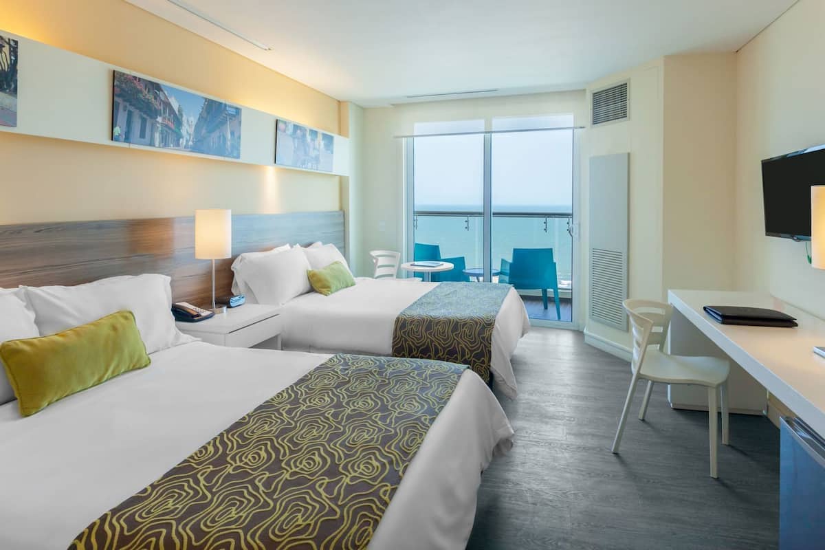 Habitación de hotel con dos camas, un escritorio, una silla, un televisor y un balcón con vistas.