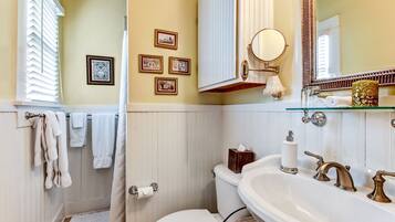 A bathroom with a toilet, sink, and shower. There are towels hanging on a rack, a mirror, and framed pictures on the wall.