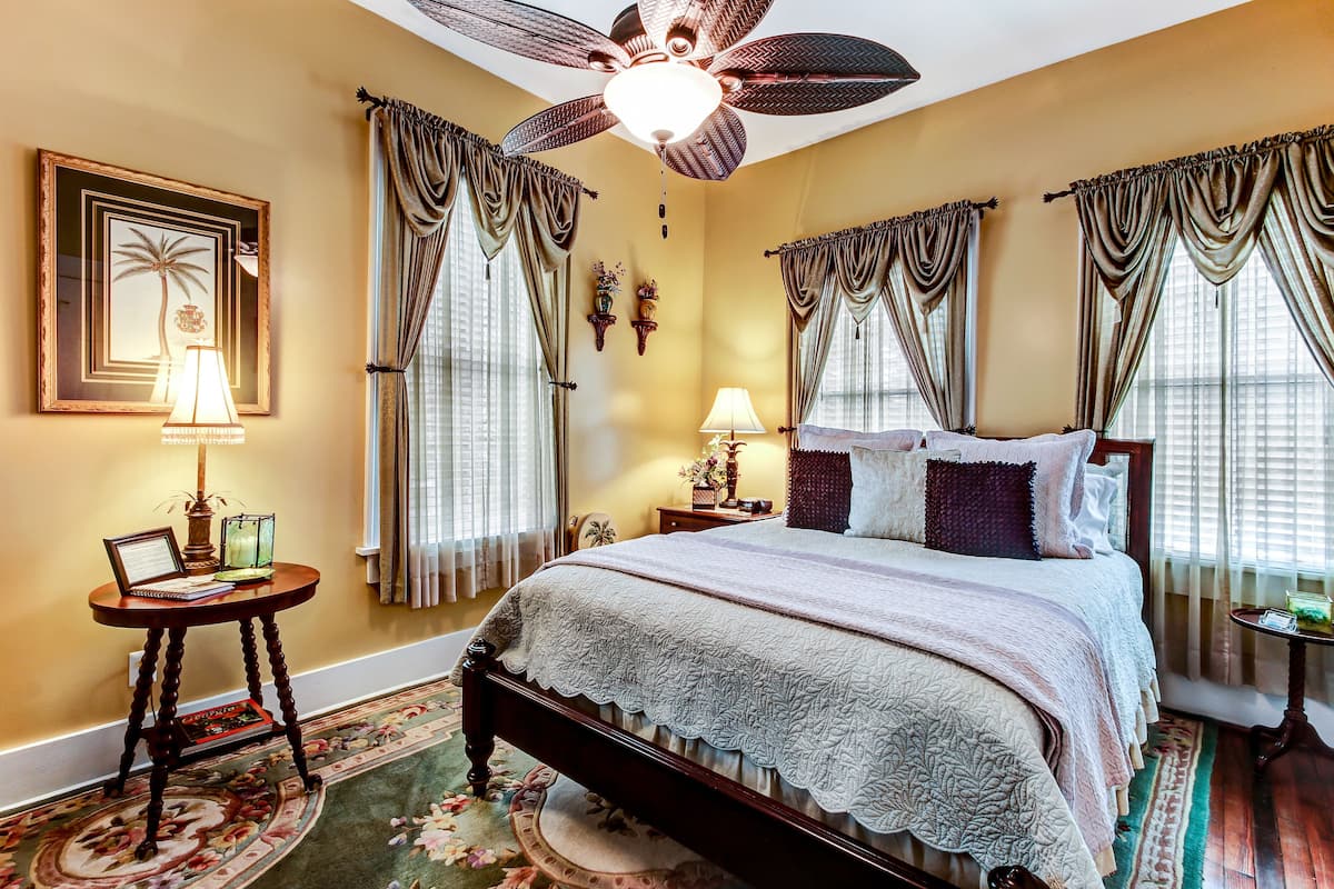 A bedroom with a large bed, a ceiling fan, and a floral carpet.