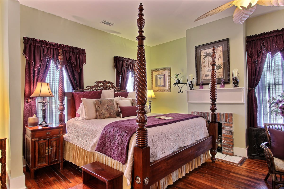 A four-poster bed with a wooden headboard, a nightstand with a lamp, and a chair with a cushion.